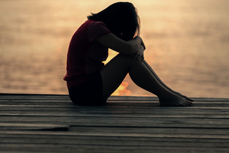 Teen sitting on dock with head on knees
