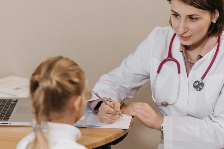 Doctor in White Lab Coat taking Notes in front of a child