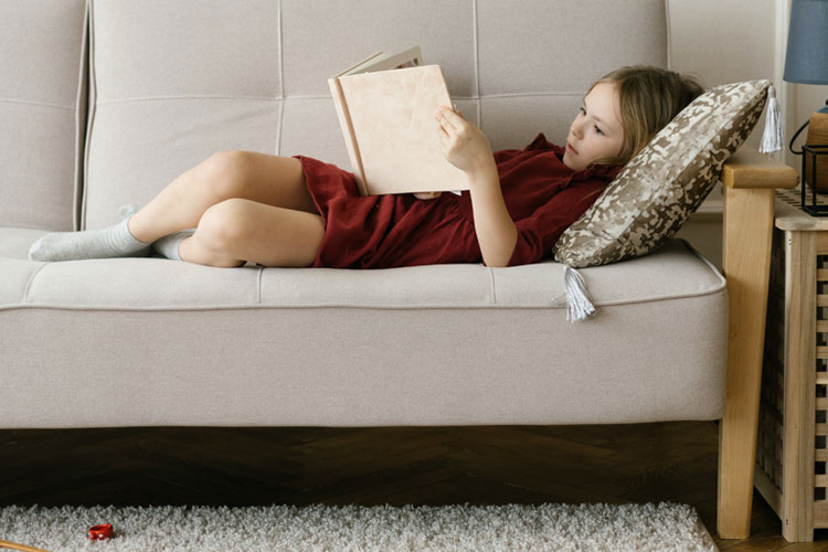 Child laying on couch reading a book