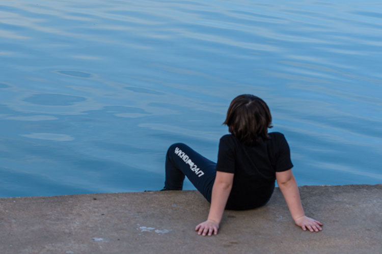 Child sitting on pier looking at the water facing away from the camera