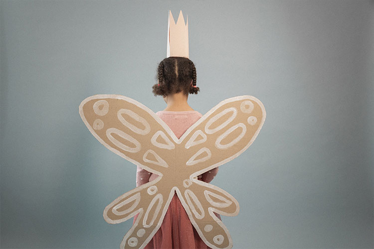 Young child facing away from camera with cardboard wings and a crown