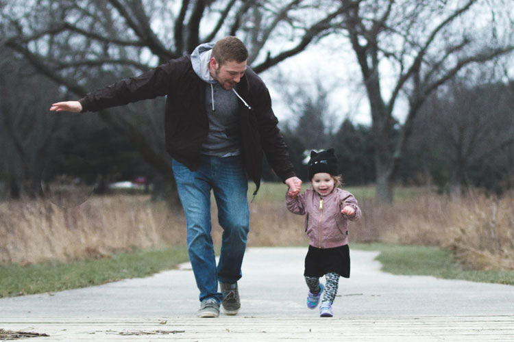 Adult and small child holding hands and walking down a path